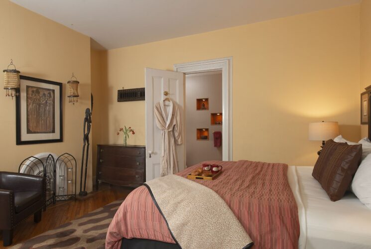 Bedroom with king bed, leather club chair, dresser, decorative artwork, and robe hanging on the door