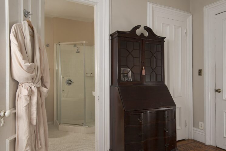 Bedroom with dark wood armoire and plush robe hanging on a doorway open to a bathroom with glass door shower