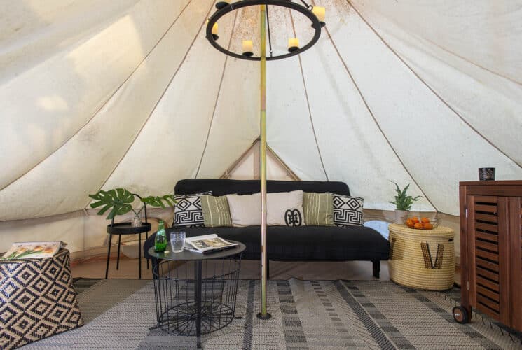 The inside of a glamping tent with a black couch, brown wood cart and coffee table