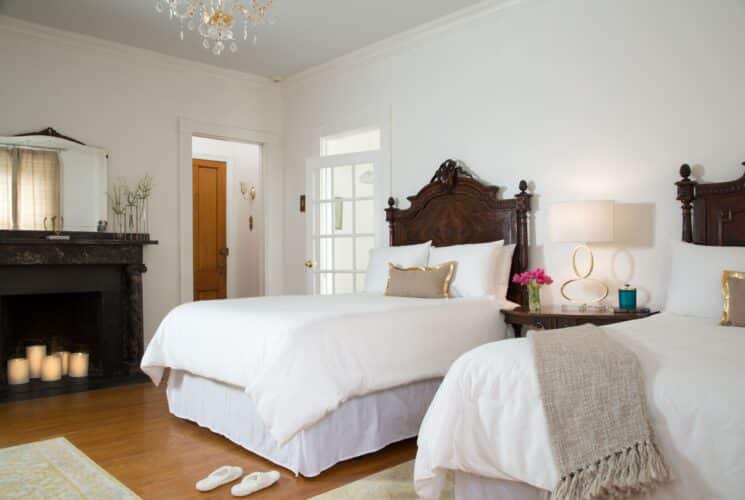 Spacious bedroom with two double beds with dark wood ornate headboards, hardwood floors and decorative fireplace