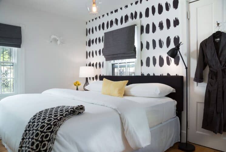 Bright bedroom with king bed, white linens, black and white wallpaper, grey robe hanging on a door