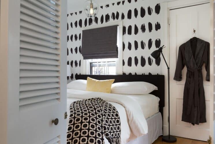 Bright bedroom with king bed, white linens, black and white wallpaper, grey robe hanging on a door