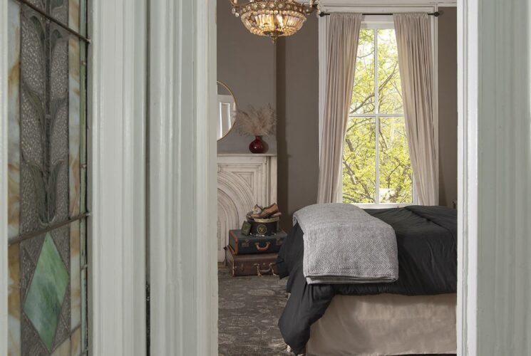 Doorway into a bedroom showing hardwood floors, bed, stack of decorative suitcases, window with curtain