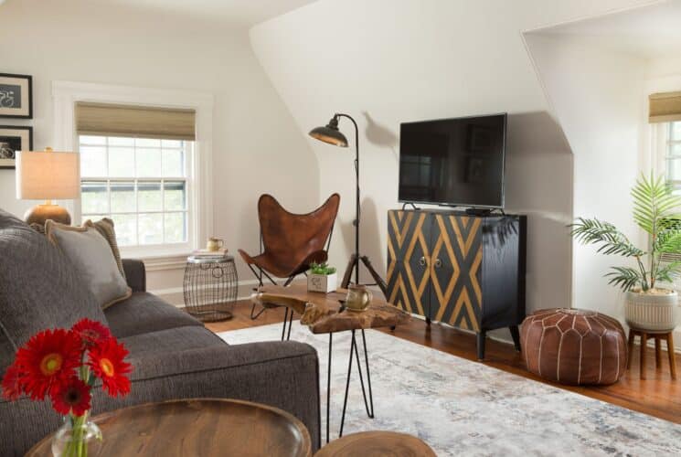 Living room with couch, dresser with TV, leather chair, large window, wood slab hair pin coffee table