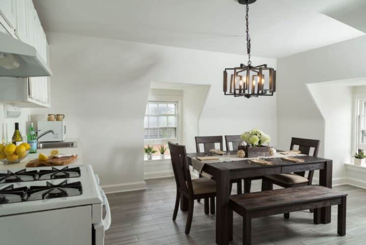 White open kitchen with dark wood table with bench and four chairs, white cabinets and countertop, two windows