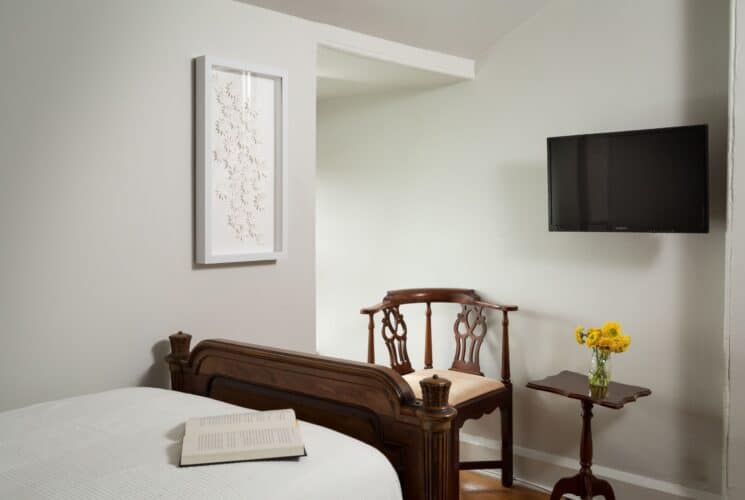 Bedroom with twin bed, sitting chair, table with vase of yellow flowers, TV hanging on the wall