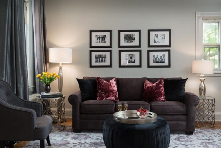 Living room with couch, chair, plush ottoman, metal side tables with lamps, gallery wall with black and white photographs