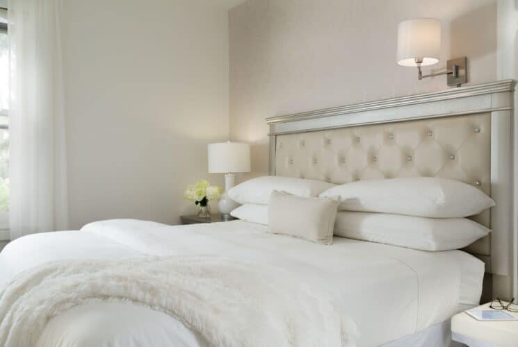 Bedroom with king bed, silver and tan headboard, white pillows and linens with a white fur throw blanket