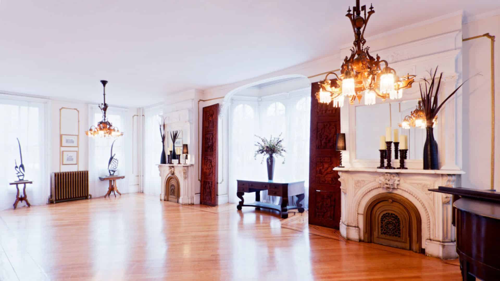 Large open room with hardwood floors, two fireplaces, chandelier, and bright windows