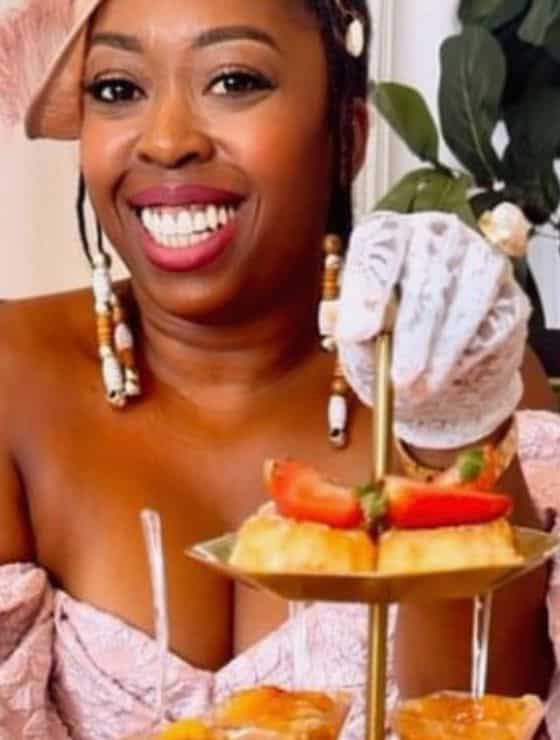 African American woman in a beautiful hat, dress, and gloves with her hand on a tiered dessert tray