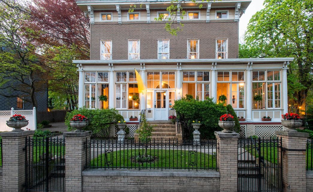 Unique two story home with covered front patio full of paned windows, lush bushes and wrought iron and brick front gate