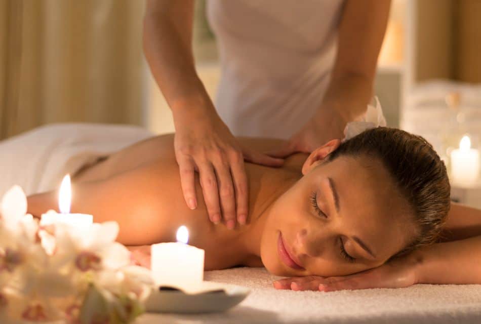 A masseuse giving a massage to a woman laying on a massage table with flowers and candles in the room