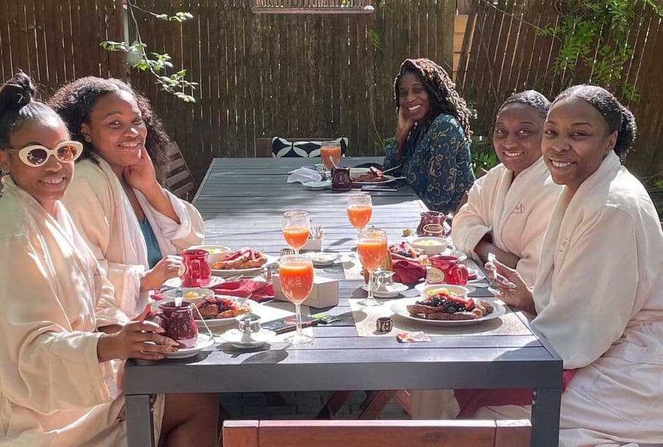 A group of ladies sitting in robes outdoors at a dining table having breakfast