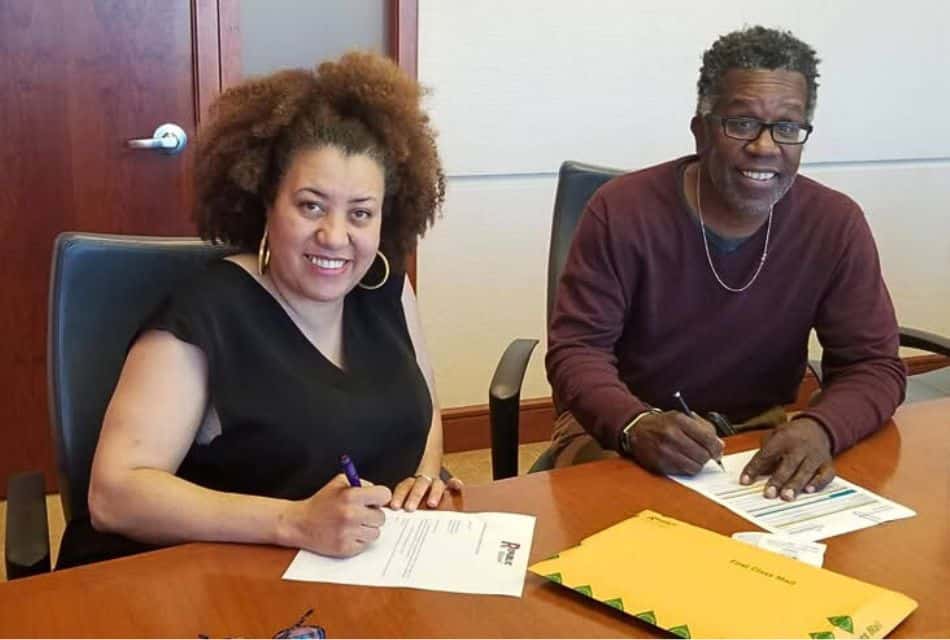 A man and woman sitting at a wood table in an office signing papers