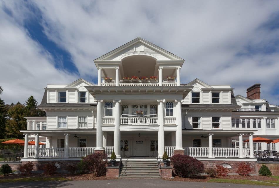 Expansive and stately white mansion with wrap around porch, tall columns, two levels of balconies and outdoor sitting areas on both sides